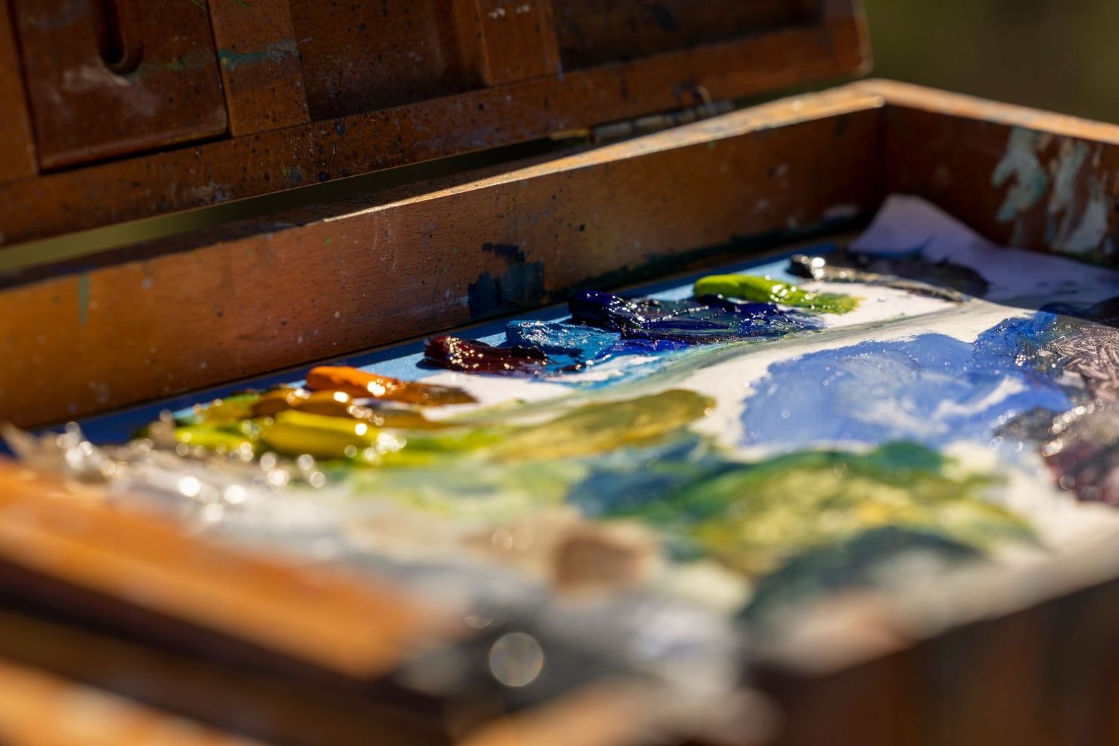 Vivid oil paints spread across a palette inside a wooden paint box