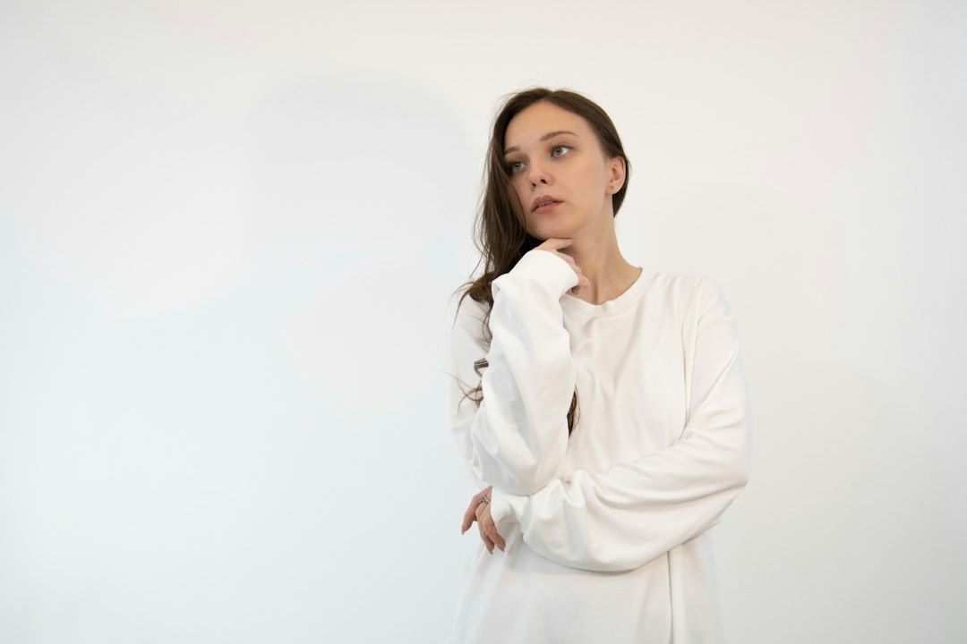 Thoughtful woman in white standing against a quiet studio wall